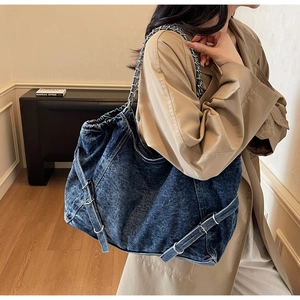 Detail of blue washed denim tote bag with silver chain strap and decorative buckle design