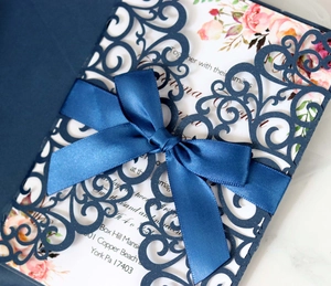 Detail of laser-cut navy wedding invitation with satin bow and floral inner page
