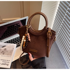 Detail of dark brown suede bucket bag with round handle and wooden beaded tassel charm