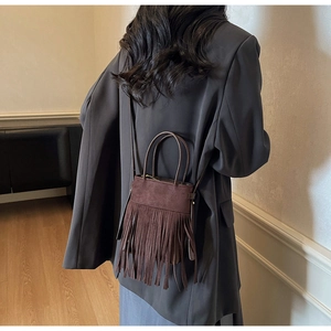 Détail du sac seau en daim marron foncé avec de longues franges et une bandoulière