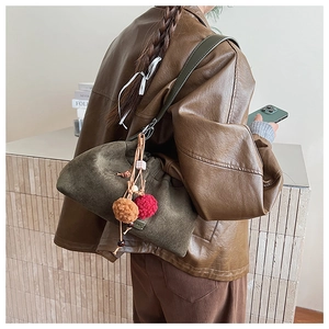 Détail du sac seau en daim olive avec des pompons en peluche sur la bandoulière