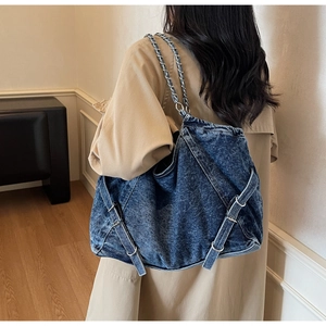 Detail of blue denim hobo bag featuring silver chain strap and decorative cross straps