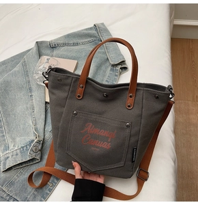 Detail of dark grey canvas tote bag featuring brown leather handles and red printed logo