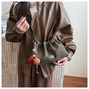 Détail du sac seau en daim vert olive orné de pompons décoratifs rouges et marron