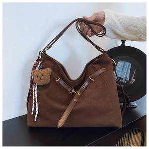 Dettaglio macro della borsa tote in pelle scamosciata marrone scuro con charm orso
