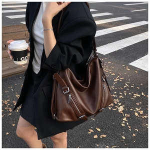 Close-up of pebble-grain brown leather tote with silver zippers in urban street setting