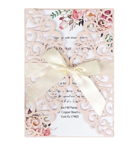 Detail of laser-cut lace wedding invitation with a beige silk bow and floral insert