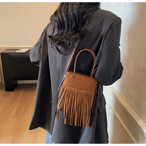 Détail d'un sac seau en daim marron foncé avec de longues franges porté par un modèle