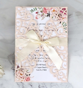Detail of laser-cut lace wedding invitation with peach cover and white satin ribbon bow