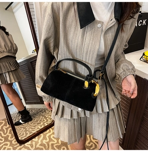 Close-up of black matte handbag featuring a unique gold-toned buckle and leather handle