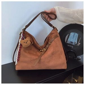 Dettaglio borsa tote in pelle scamosciata marrone con tracolla e ciondolo a orso