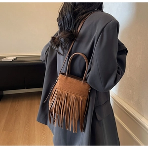 Sac seau en daim marron à longues franges porté par un mannequin dans un décor minimaliste