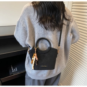 Detail of black suede bucket bag with colorful bead charm and metal logo on grey sweater