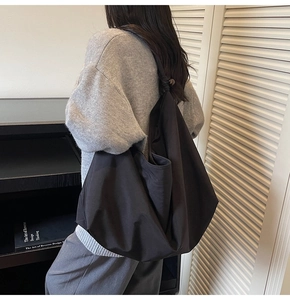 Detail of minimalist black oversized shoulder bag with knotted strap and soft fabric texture