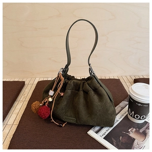 Détail du sac seau en daim vert avec pompon décoratif et perles en bois sur une table