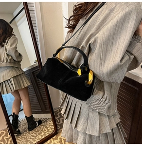 Detail of a black suede cylinder bag featuring gold metal rings and a sleek zipper