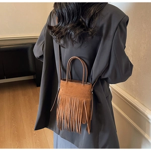 Sac seau en daim marron avec de longues franges porté par un mannequin en extérieur