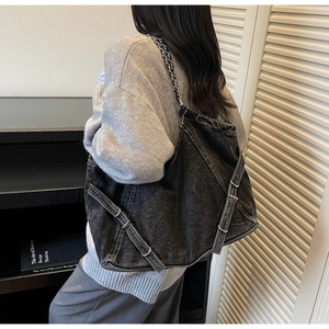 Detail of a large washed denim tote bag with metal chain strap worn by a model