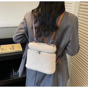 Close-up of white plush backpack featuring brown leather straps and silver zipper details