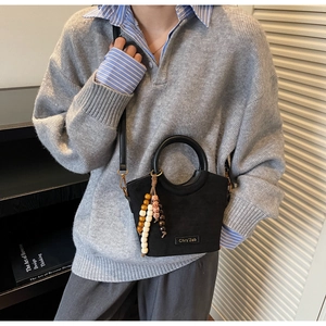 Detail of black bucket bag with wooden bead charm and branded plaque shown on model