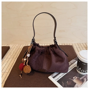 Détail du sac seau en daim marron foncé avec design plissé et pompons décoratifs