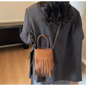 Détail du sac seau en daim marron avec de longues franges porté à l'épaule par un mannequin
