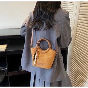 Detail of a brown suede bucket bag with round handles and wooden bead pendant accessory