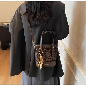 Leopard print bucket bag with gold logo, beaded charm, and leather trim details