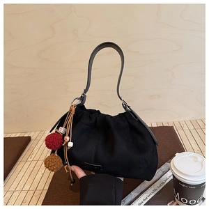 Détail du sac seau en daim noir avec fermeture à cordon et breloques décoratives