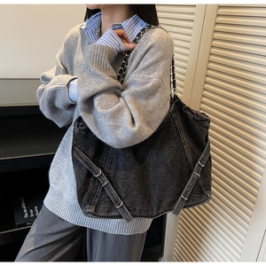 Detail of a large black washed denim tote bag with metal chain strap worn by a model
