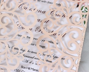 Close-up of laser-cut lace wedding invitation with pearlescent pink floral pattern