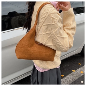 Close-up of brown suede shoulder bag with minimalist curved design worn by a model