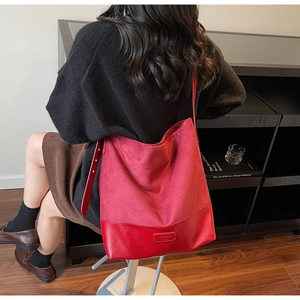 Detail of red suede and leather tote bag showing wide strap and brand logo plate