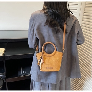 Detailed back view of a brown suede bucket bag with beaded charm and wooden handle