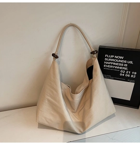 Detail of beige shoulder bag featuring rustic wooden beads and textured fabric finish
