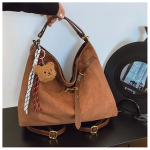 Dettaglio di una borsa a spalla in pelle scamosciata marrone con ciondolo a orsetto