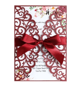Detail of burgundy laser-cut lace wedding invitation with ribbon and floral insert