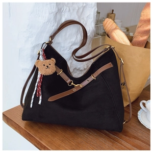 Dettaglio di borsa tote in pelle scamosciata nera con manici marroni e ciondolo orso