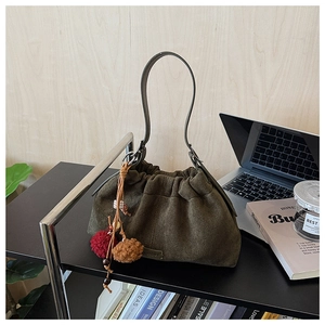 Détail du sac seau en daim vert foncé avec fermeture à cordon et breloques ethniques