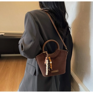 Detail of dark brown matte bucket bag with circular wooden handle and beaded tassel