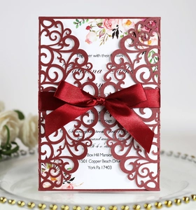 Detail of laser-cut burgundy lace wedding invitation with ribbon bow on elegant glass plate
