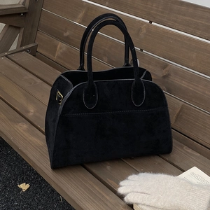 Dettaglio di borsa ventiquattrore in camoscio nero con fibbie dorate su panca in legno