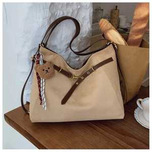Dettaglio di una borsa tote in pelle scamosciata beige con cinturini in pelle e orsetto
