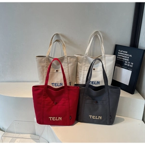 Détail de quatre sacs fourre-tout en toile colorés avec poches avant et broderie TELN