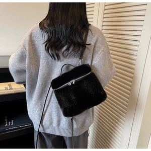 Back view of a model wearing a plush black faux fur crossbody bag with leather strap