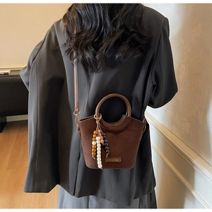 Detail of dark brown suede bucket bag with wooden bead charm and round metal handle