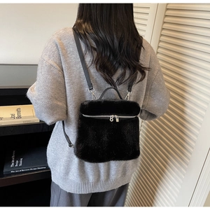 Detail of a soft black faux fur backpack featuring silver zippers and slim faux leather straps