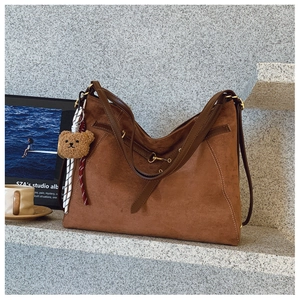 Dettaglio della borsa tote in pelle scamosciata marrone con tracolla e ciondolo orsetto