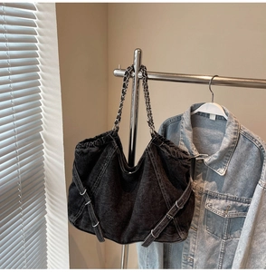 Detail of black denim tote with white contrast stitching and metal chain shoulder strap