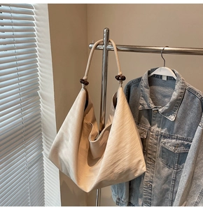 Detail of beige hobo bag strap featuring dark brown wooden bead accents and soft texture